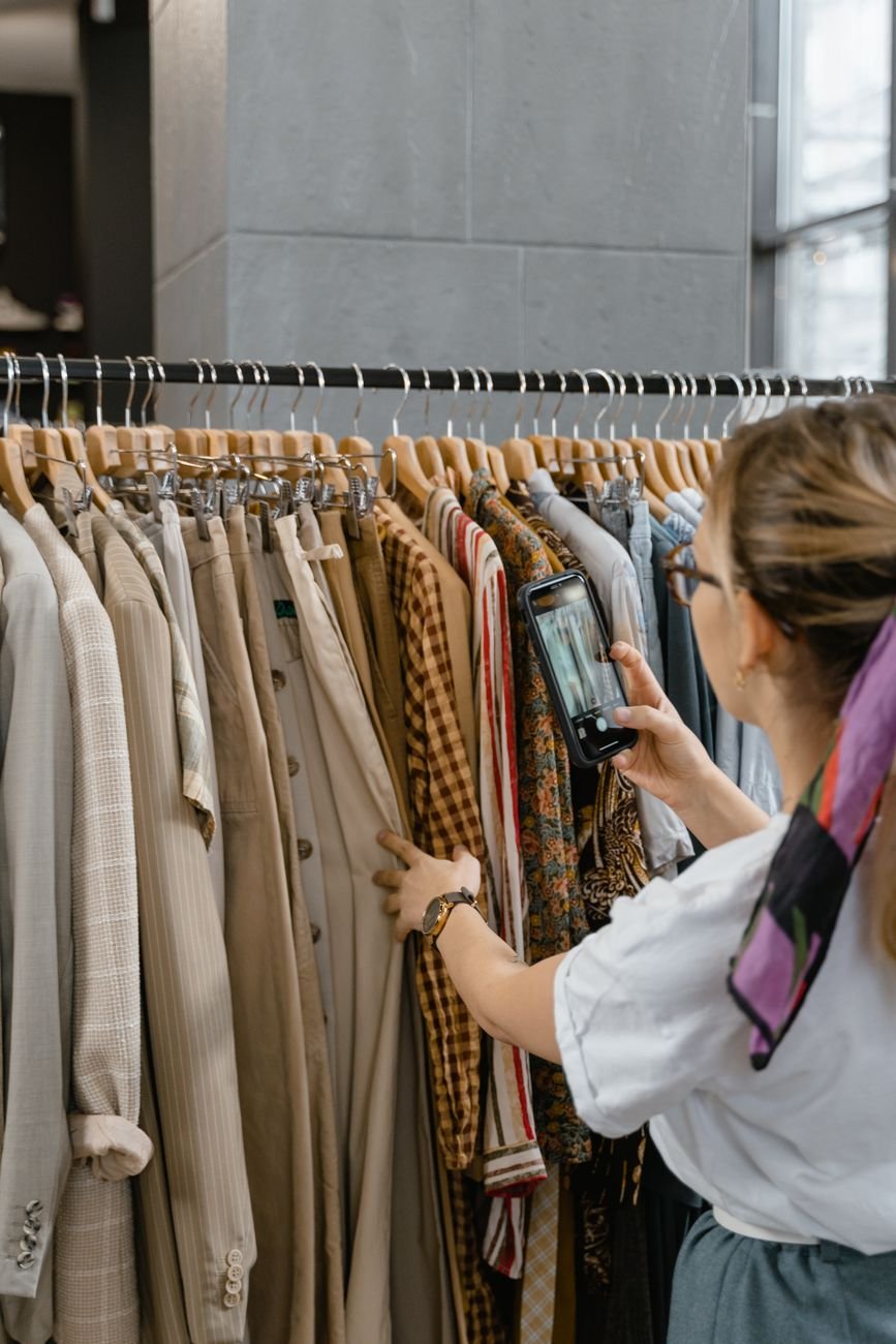 A woman using a smartphone to photograph stylish clothes in a boutique setting